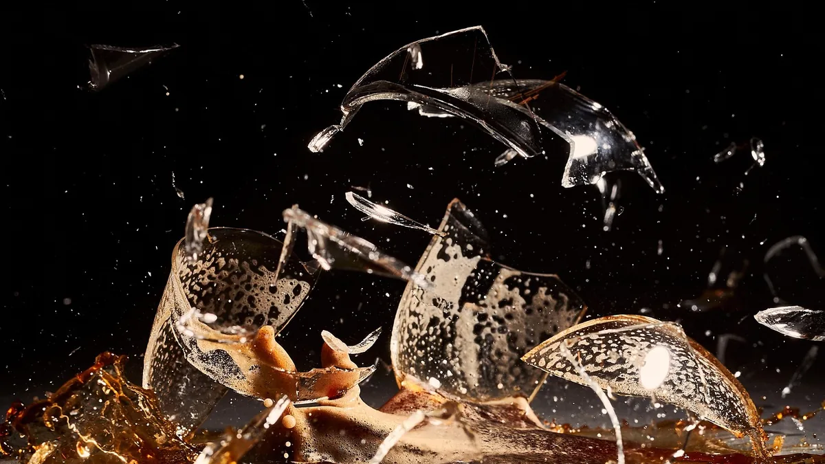 High-speed shot of a glass shattering into pieces with amber liquid splashing against a dark background.