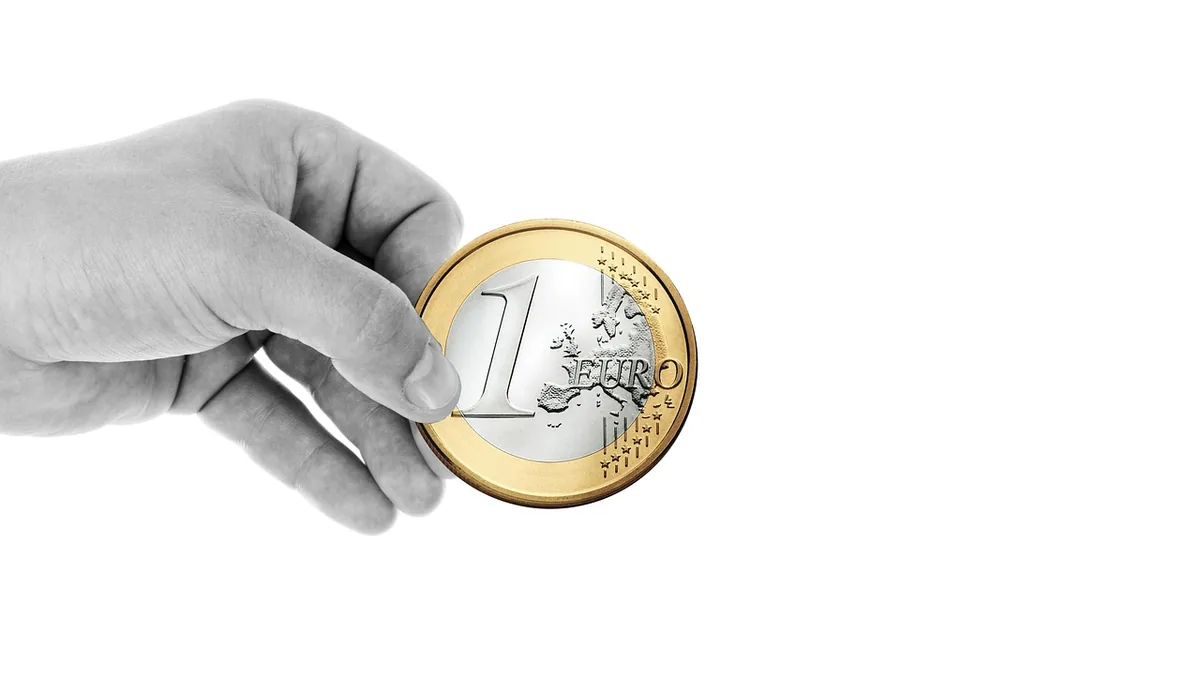 A grayscale hand holding a single one-euro coin against a white background.