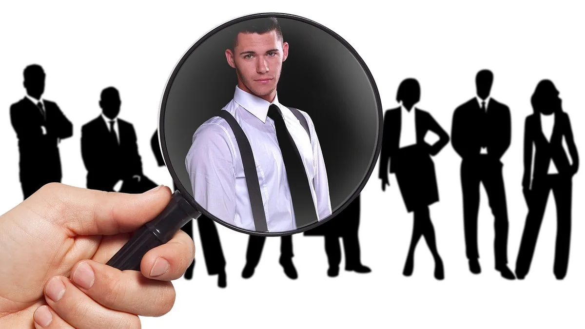 Magnifying glass focusing on a single male candidate in a shirt and tie, surrounded by silhouette figures.