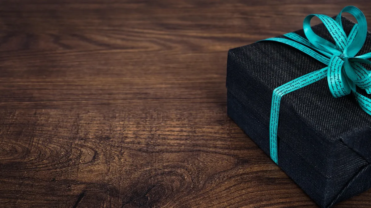 Black gift box tied with a teal ribbon printed with cursive text, on a dark wooden table.