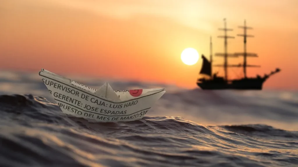 A paper boat made from a Spanish document floats on ocean waves under a warm sunset sky.