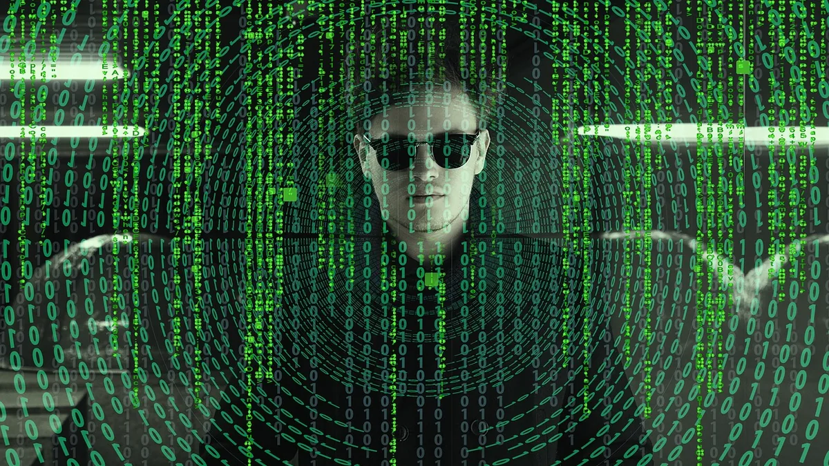A man in sunglasses behind a green overlay of cascading binary code, symbolizing a cyber attacker.