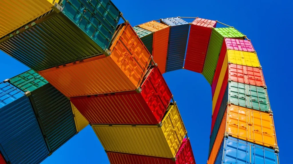 A colorful arch of stacked shipping containers against a bright blue sky, symbolizing complex supply chains.