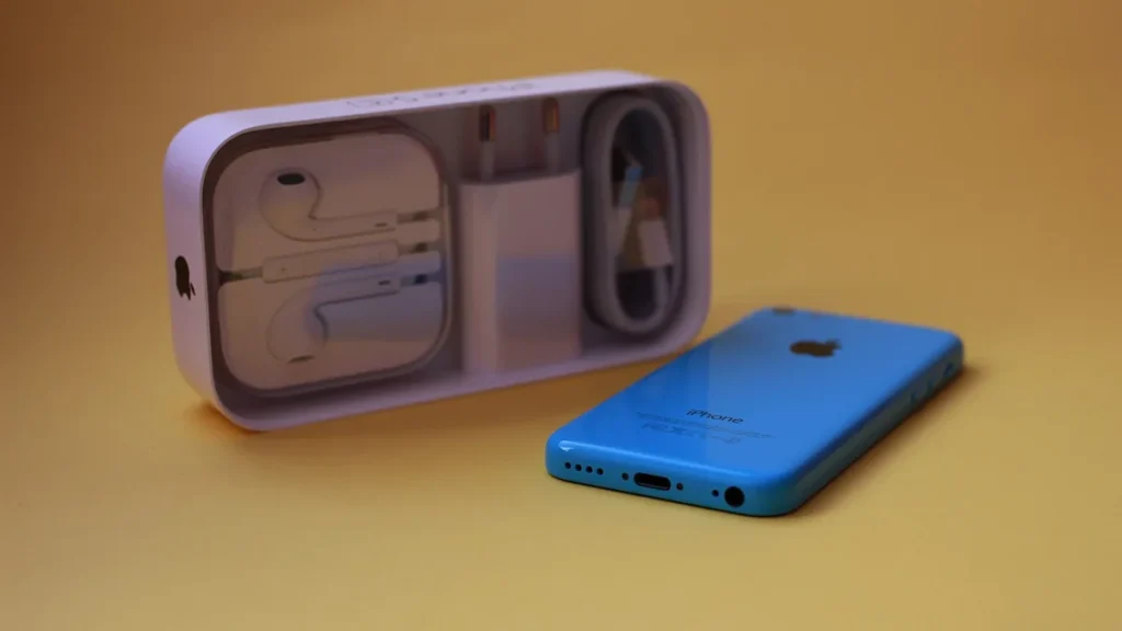A blue iPhone 5c next to its box containing EarPods, a charger, and a cable on a yellow background.