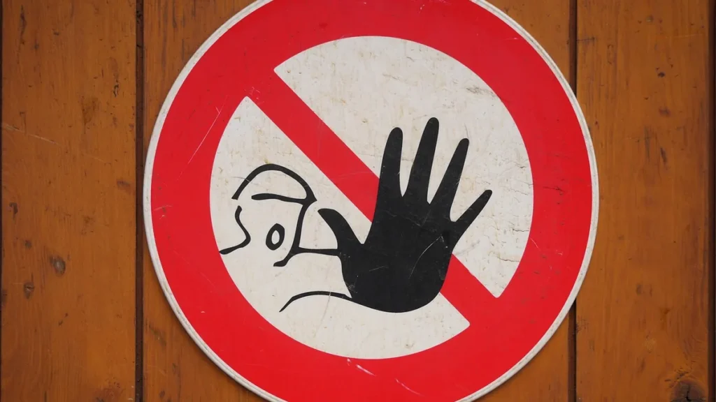 A red circular prohibition sign with a black hand and a stylized face on a wooden surface, representing a stop or warning.
