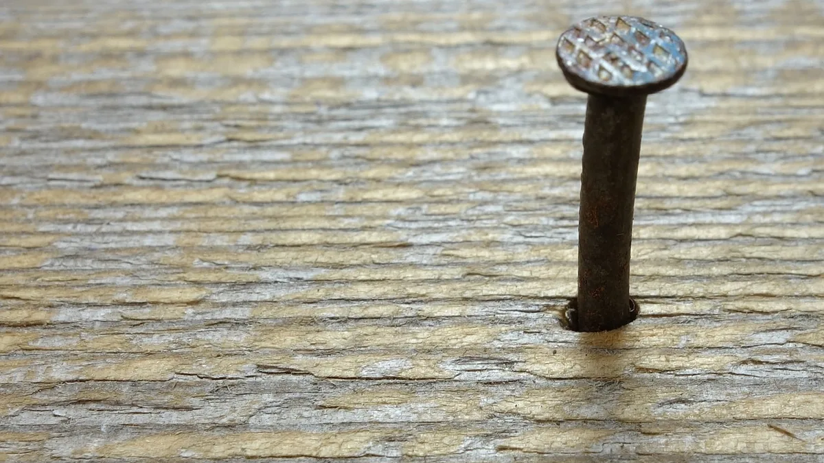 A close-up of a rusty nail head sticking out of a weathered wooden board.