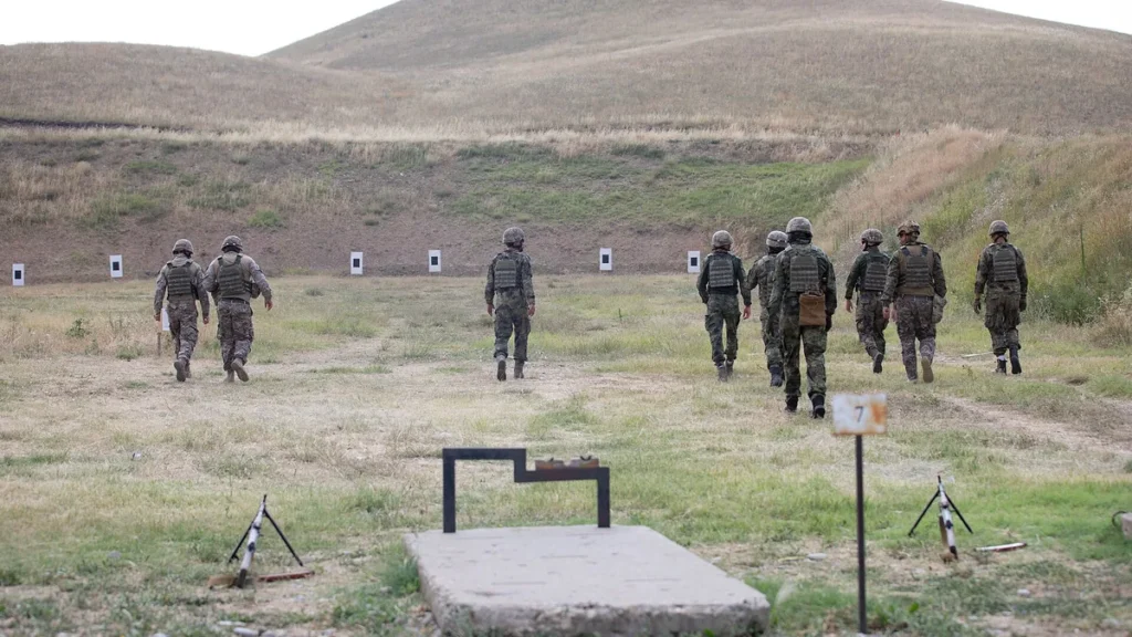 Soldiers in military gear walking towards targets on a grassy shooting range.