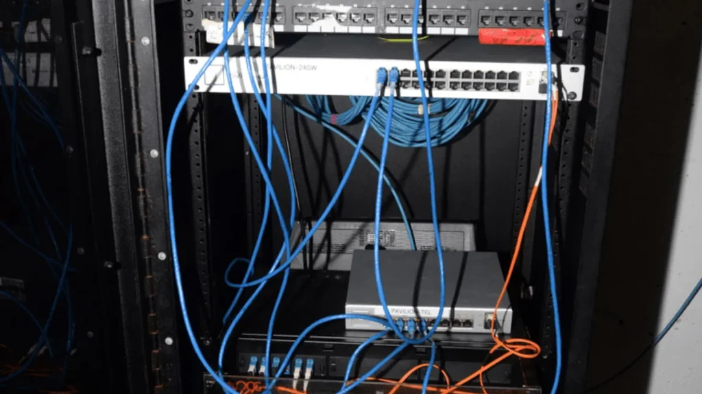 Blue network cables dangle from switches in a dark server rack, symbolizing complex network infrastructure.