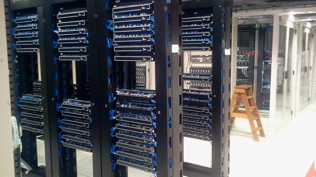 Server racks with neatly organized blue cables in a data center, with a wooden ladder nearby.