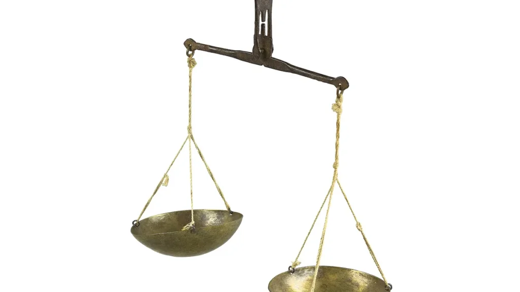 An antique brass hanging balance scale tilted unevenly against a white background.