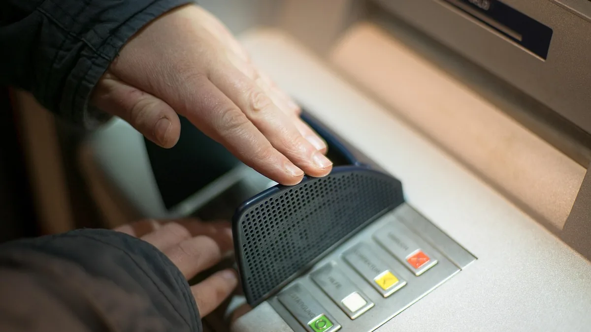 A hand shields the keypad of an ATM during a transaction, symbolizing financial security and privacy.
