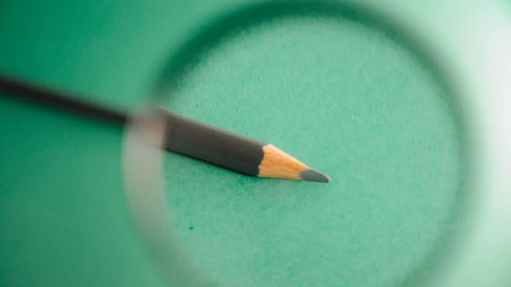 A pencil tip viewed through a magnifying glass on a green background, symbolizing close investigation.