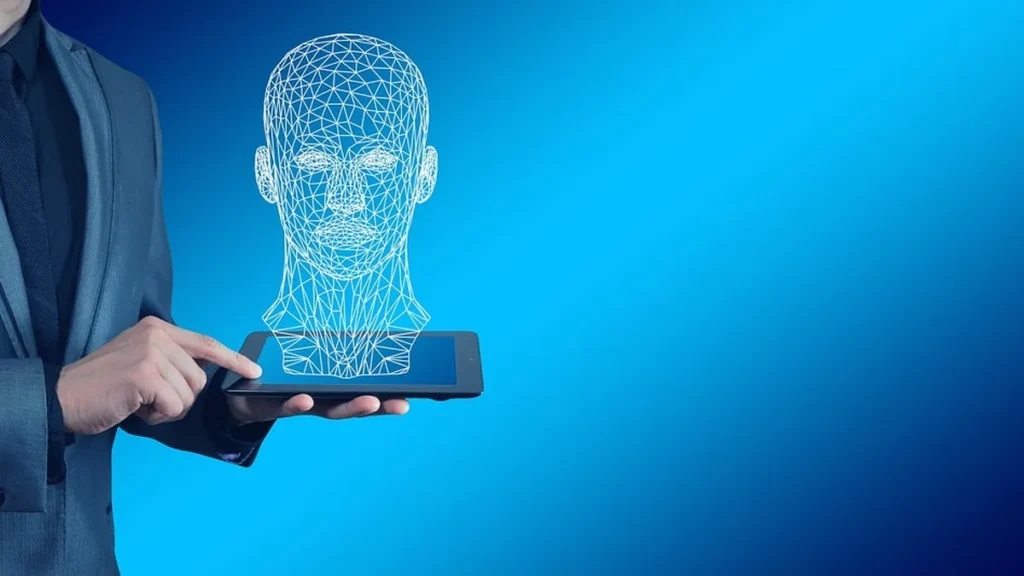 A businessman holds a tablet showing a glowing wireframe hologram of a human head against a blue background.