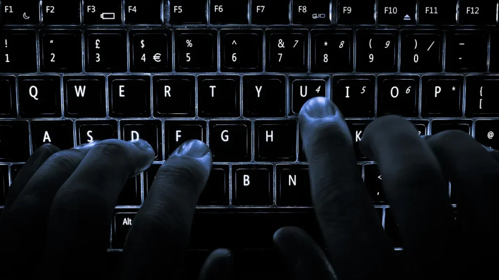 Close-up of hands typing on a glowing blue backlit keyboard in a dark room.