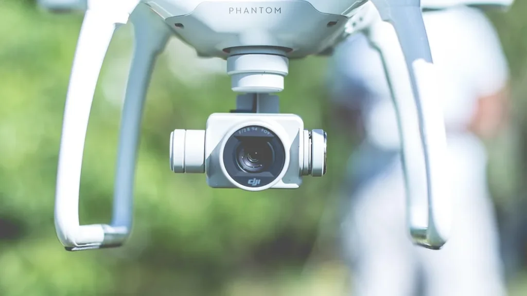 A close-up of a white DJI Phantom drone camera with a blurry green background.