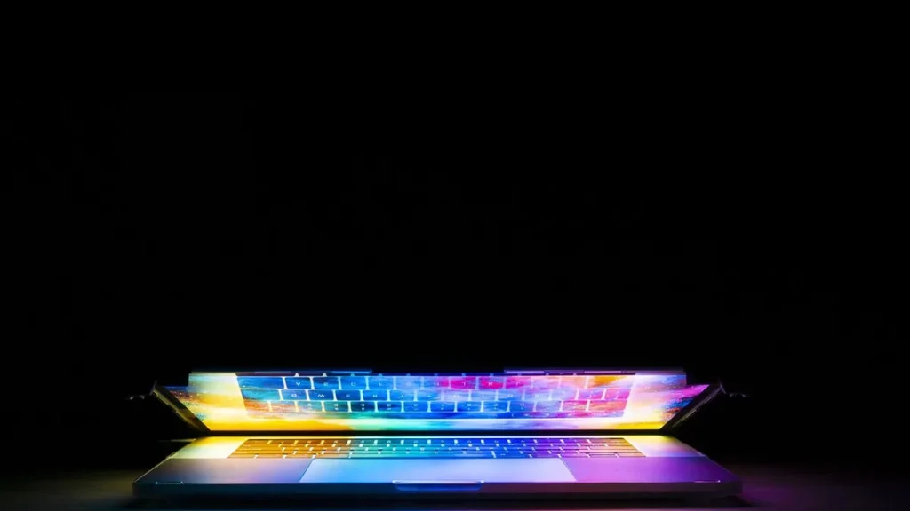 A laptop with a keyboard illuminated by colorful, vibrant rainbow-colored light against a black background.