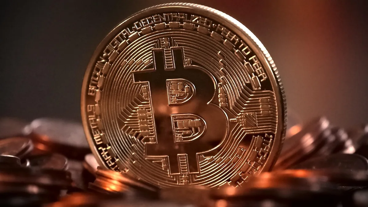 Close-up of a shiny gold-colored physical Bitcoin token standing on a pile of other coins under warm light.
