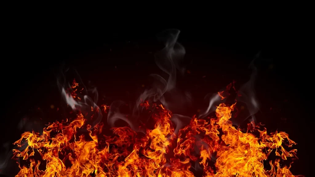 Bright orange and yellow flames with rising grey smoke against a dark black background.