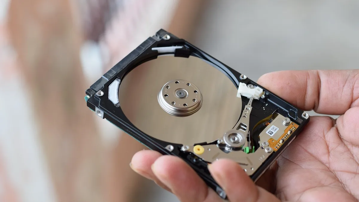 An open hard disk drive held in a hand, showing the shiny platter and internal read/write head.
