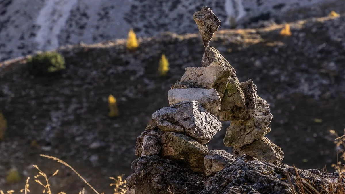 A stack of grey rocks balanced precariously on a rocky hillside with yellow trees in the background.