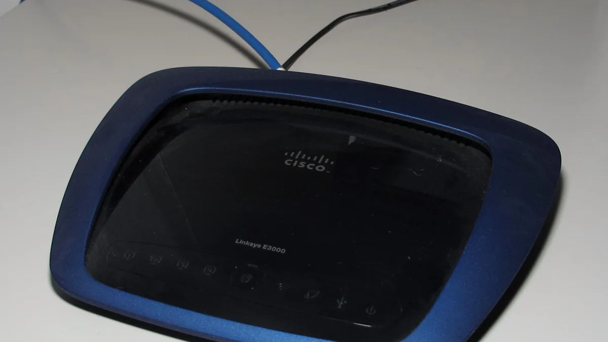 A blue and black Cisco Linksys E3000 router on a white surface with cables connected.