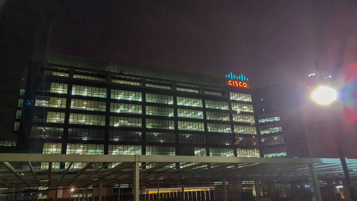 A large office building illuminated at night with a glowing Cisco logo on top.