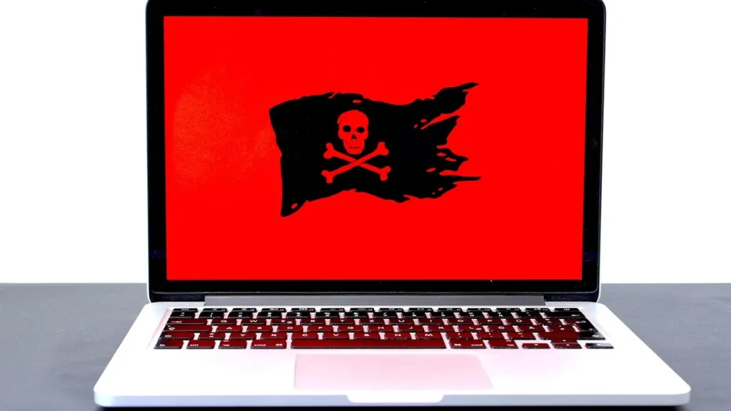 Laptop displaying a red screen with a black pirate flag and skull, symbolizing ransomware.