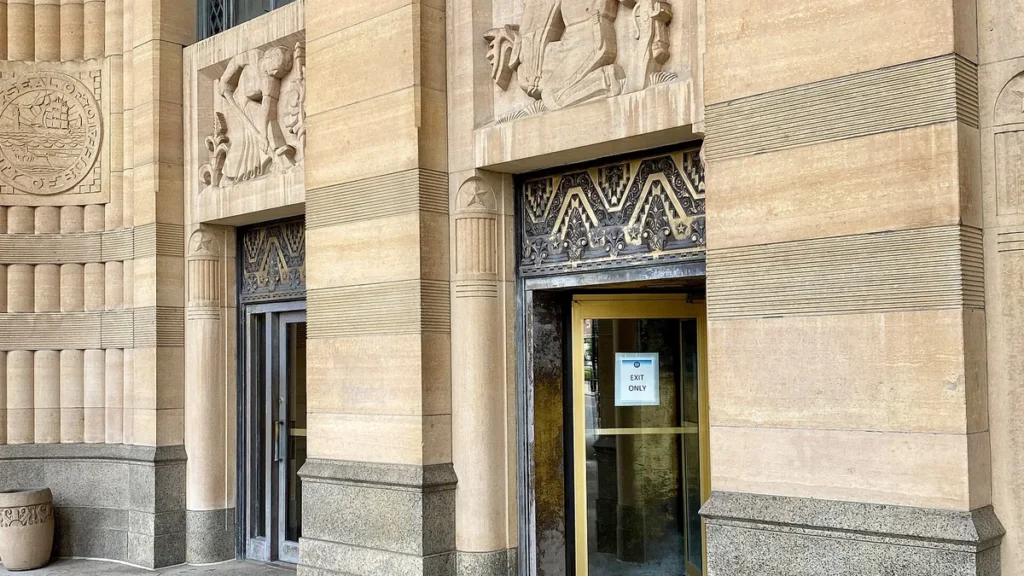 Art deco city hall entrance with a yellow-framed glass door showing an 'EXIT ONLY' sign.