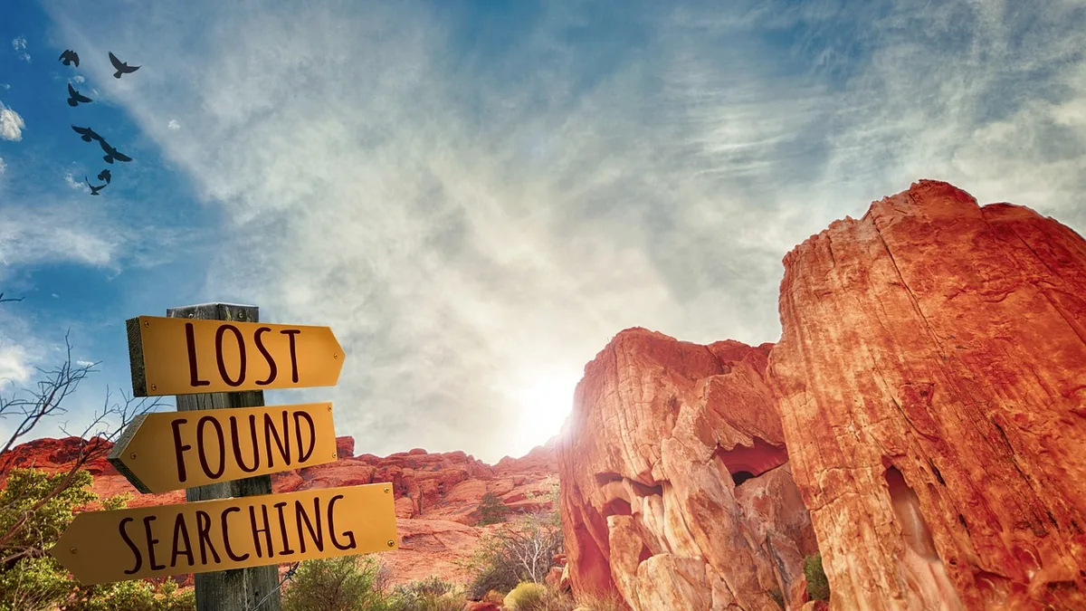 A wooden signpost pointing to 'LOST', 'FOUND', and 'SEARCHING' against red rock formations and a bright blue sky.