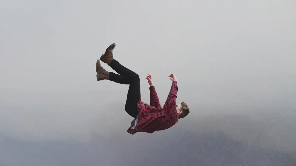 Man in red plaid shirt falling backwards in mid-air against a foggy grey background.