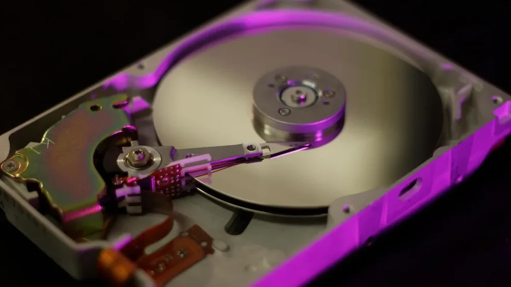 Close-up of an open hard drive platter and actuator arm under vibrant purple neon lighting.