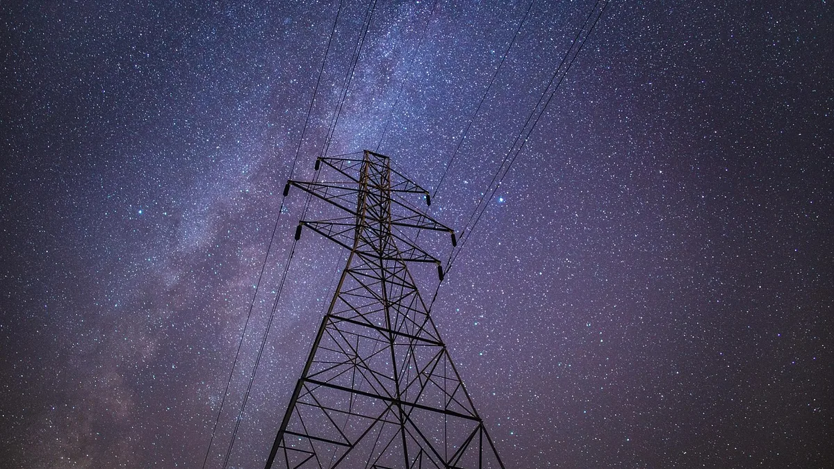 A steel power transmission tower silhouetted against a vibrant starry night sky with the Milky Way.