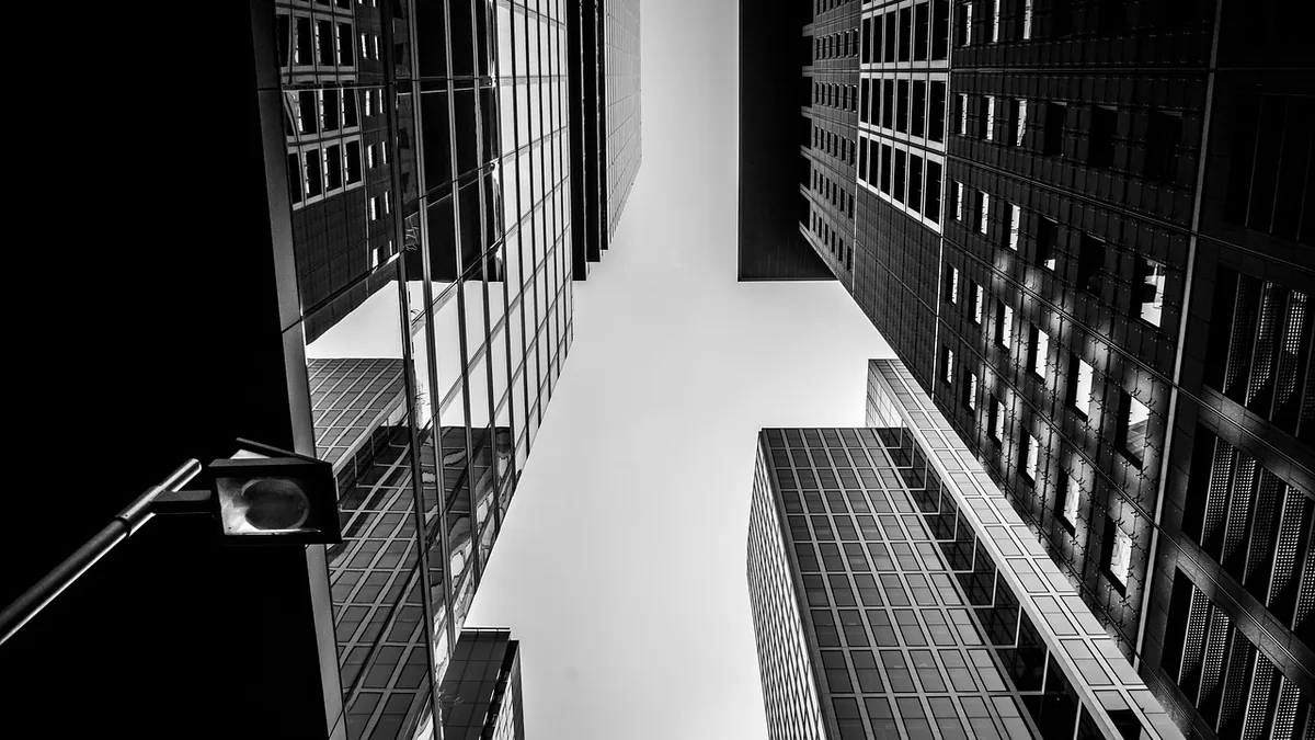A black and white low-angle shot looking up at several high-rise skyscrapers against a light sky.