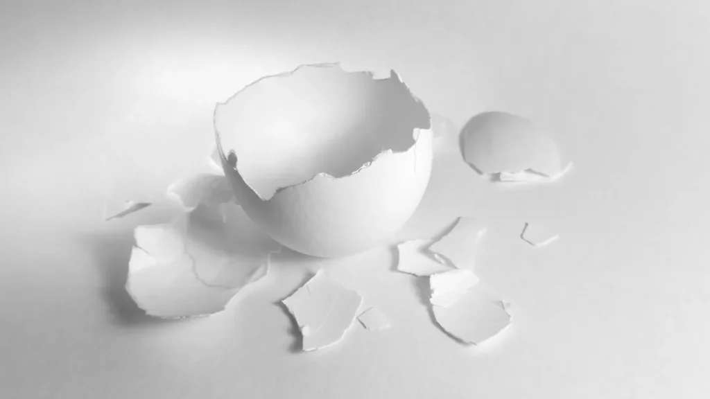 Cracked white eggshell with pieces scattered on a white surface, representing broken security.