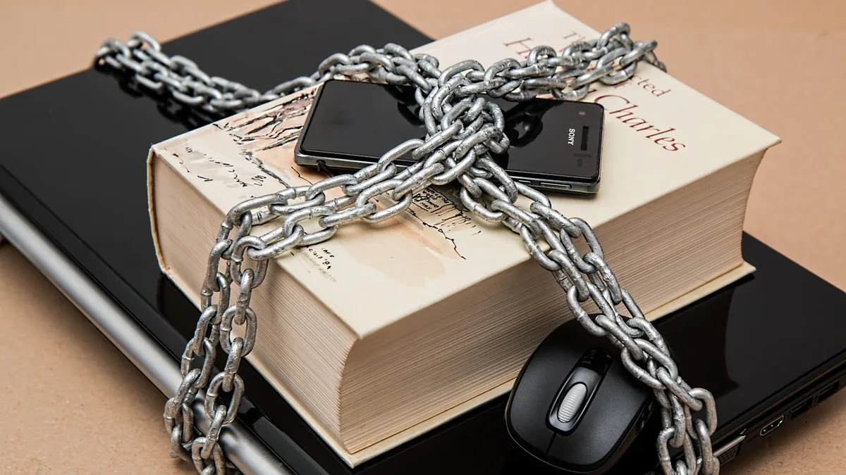 A smartphone, book, laptop, and mouse wrapped in heavy metal chains symbolizing data security.