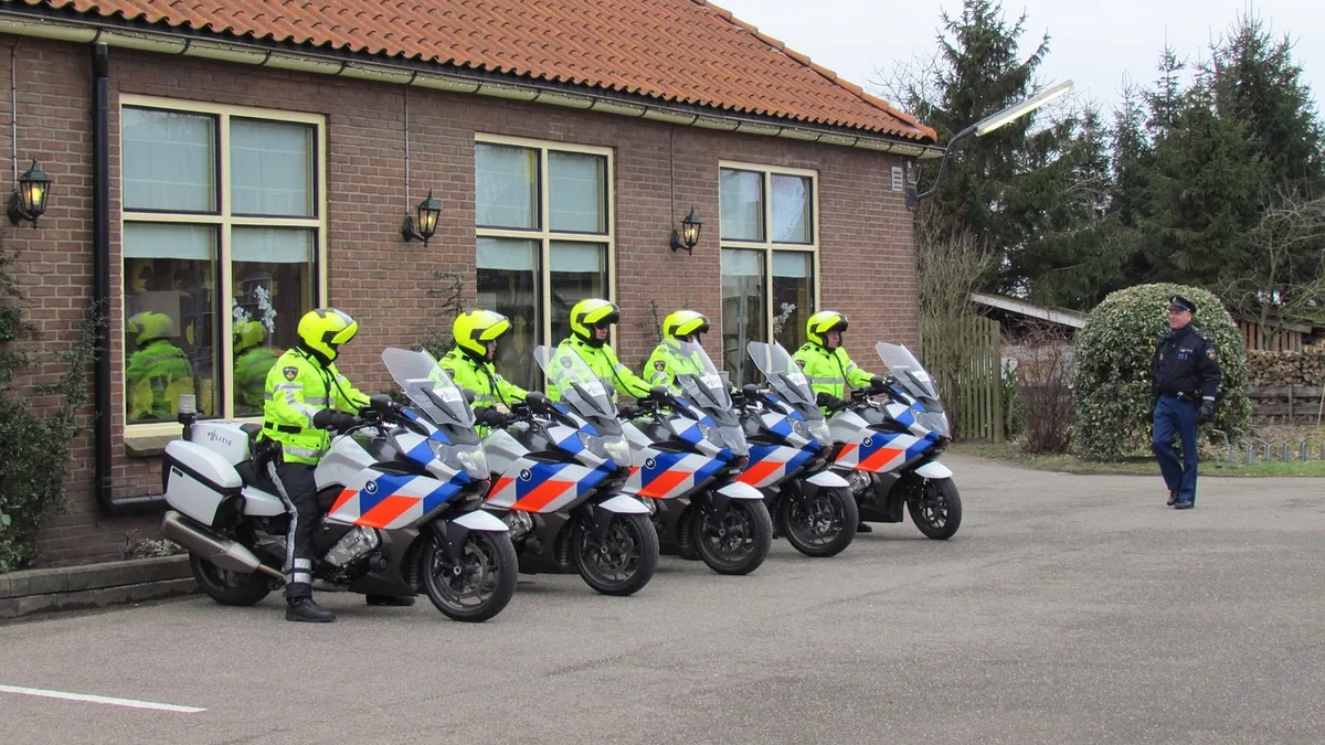 Five Dutch police officers on motorcycles lined up in front of a brick building.