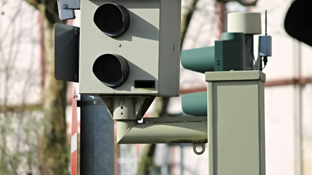 A close-up of a grey automated surveillance camera system mounted on a metal pole.