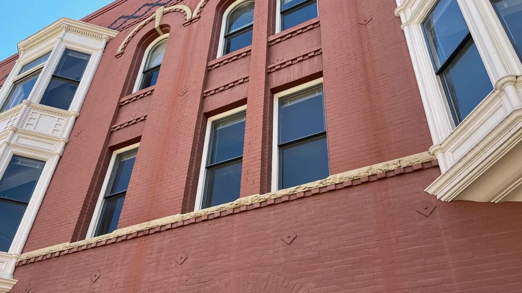 Low-angle view of a red brick building facade with white-framed windows under a blue sky.