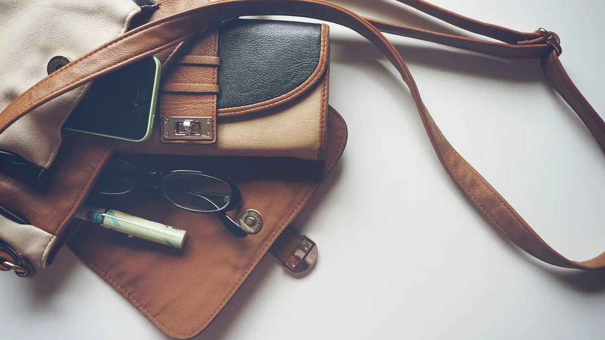 A spilled brown purse showing a smartphone, wallet, glasses, and other personal items on a white surface.