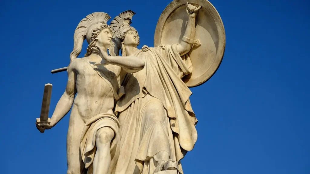 Marble statue of Athena protecting a warrior with a shield against a clear blue sky.