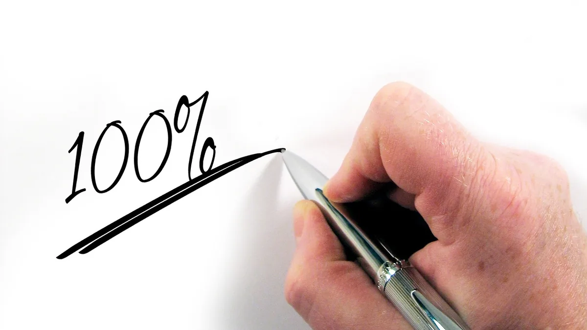 A hand writing '100%' with a silver pen on a clean white surface.