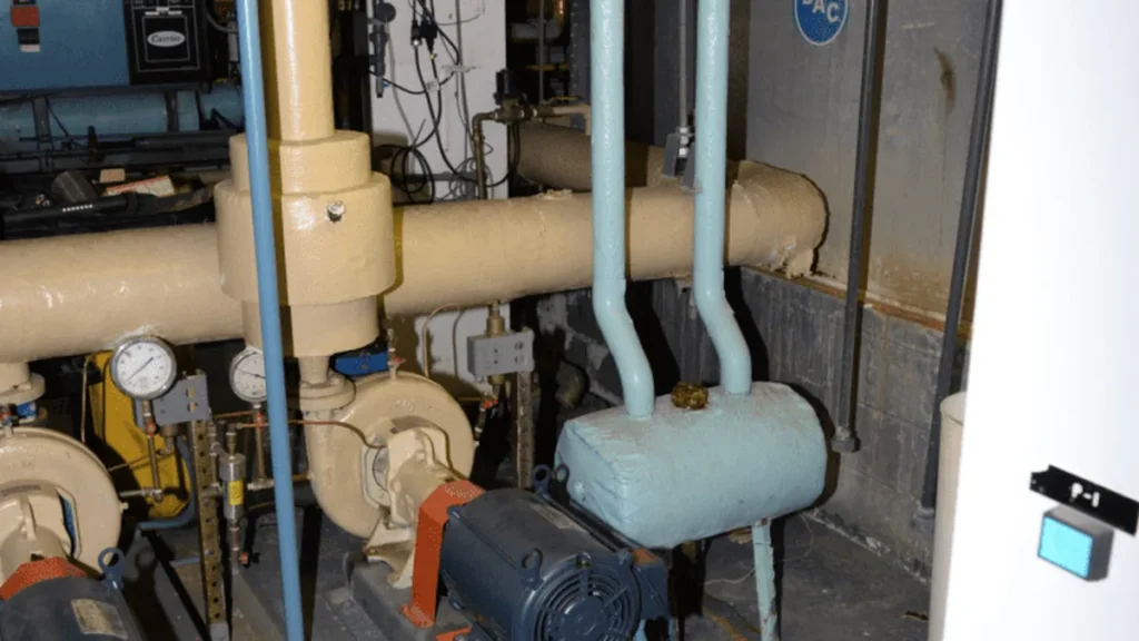 Industrial pipes, pressure gauges, and pump motors inside a facility representing critical infrastructure controls.