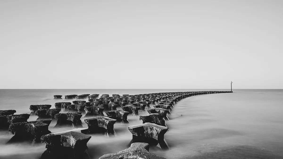 Concrete sea defense blocks stretching into the calm ocean in minimalist black and white.