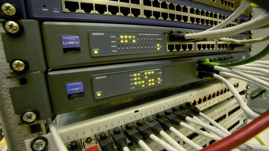 Close-up of network switches in a rack with ethernet cables and glowing status lights.