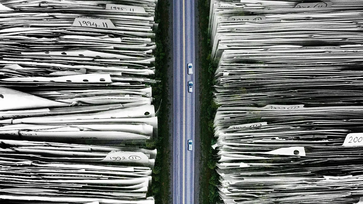 A road divides giant stacks of paper files labeled with years, visualizing massive data archives and timelines.