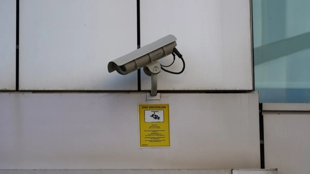 A grey Bosch security camera mounted on a wall above a yellow 'Zona Videovigilada' sign.