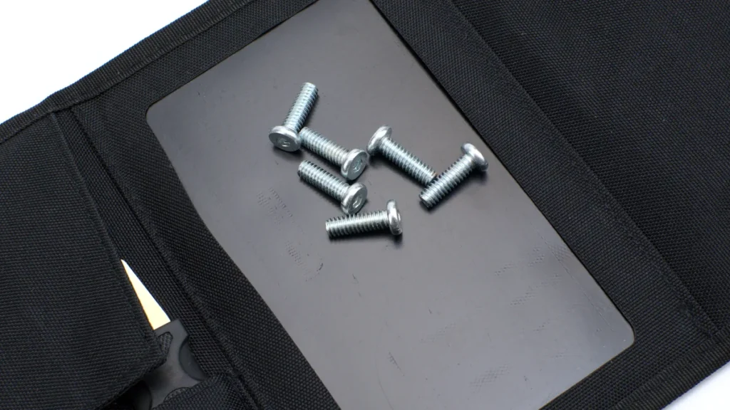 Six silver screws lie on a grey magnetic sheet inside a black fabric tool organizer.