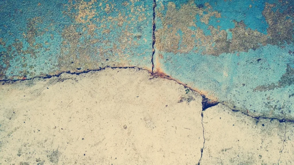 A textured wall with peeling blue paint and a prominent crack running horizontally and vertically across the surface.