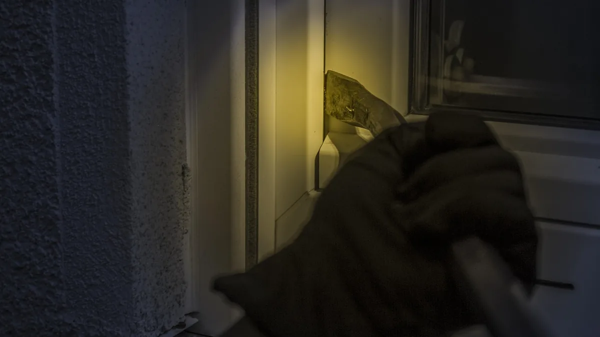 Gloved hand holding a crowbar to pry open a window, symbolizing a physical break-in or security breach.