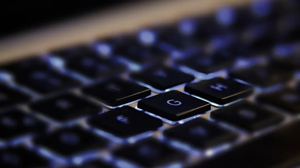 Close-up of a glowing blue backlit keyboard focusing on the G key in the dark.